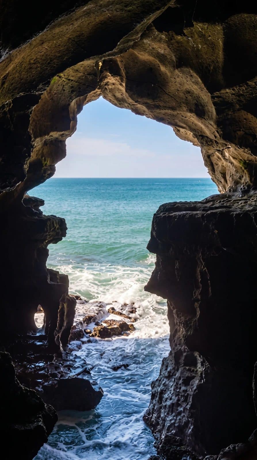 A close, straight-on view through the Map of Africa opening at the Caves of Hercules, with waves breaking on the rocks below